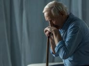 Senior sad man leans on a cane while sitting on sofa